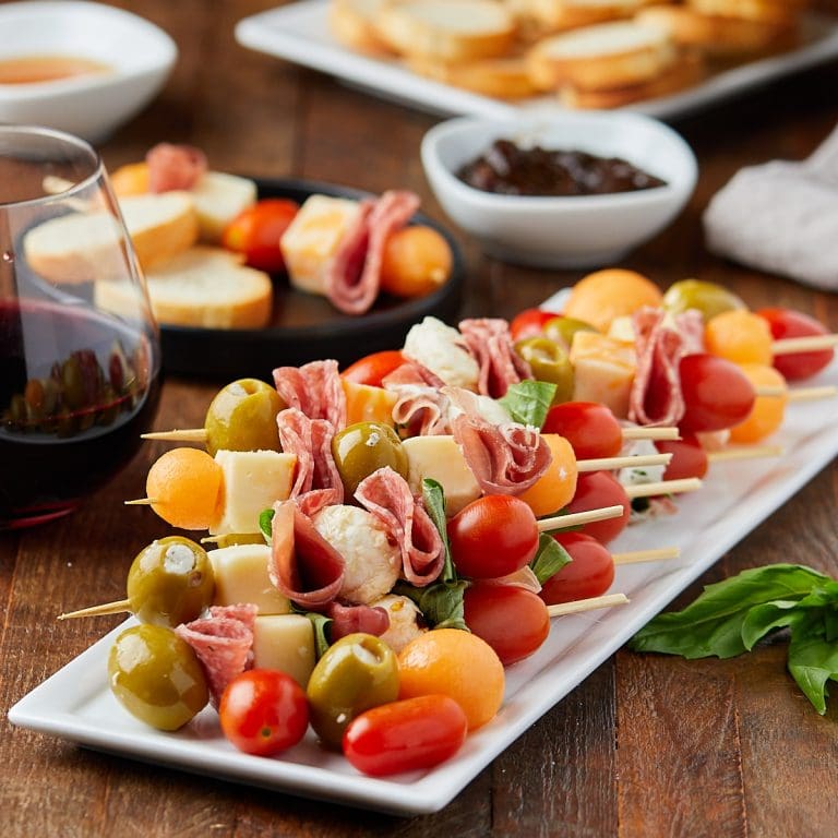 charcuterie skewers on a white plate along with a glass of wine and fig jam dipping sauce.