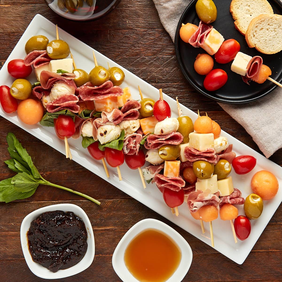 charcuterie skewers on a white plate along with a glass of wine and fig jam and honey dipping sauce.