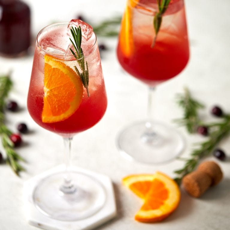 cranberry aperol spritz in a wine glass garnished with an orange slice and rosemary.