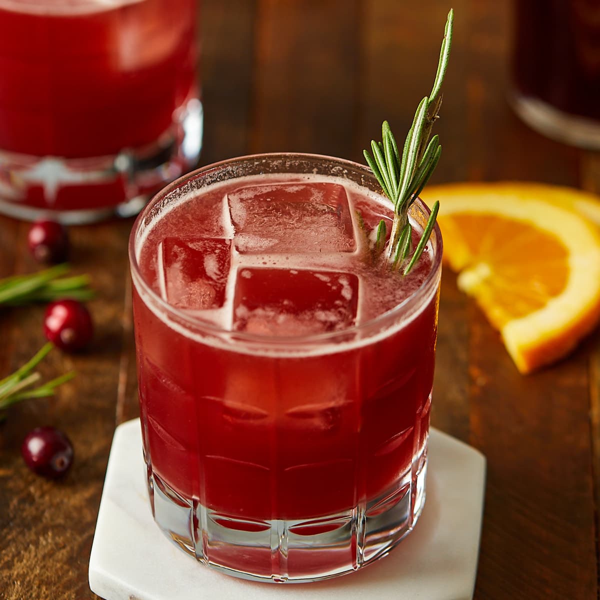 cranberry orange whiskey sour in a glass garnished with a sprig of rosemary.