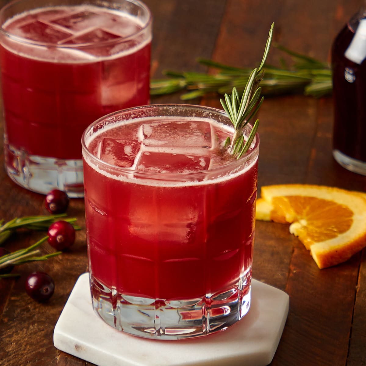 cranberry orange whiskey sour in a glass garnished with a sprig of rosemary.