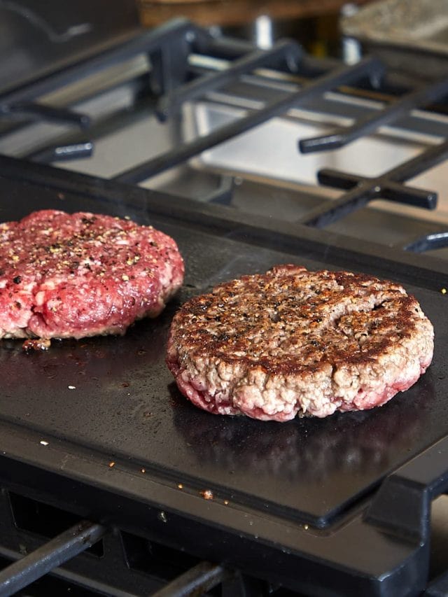 three hamburger patties grilling on a flat top with one of them flipped over and cooking on the other side.