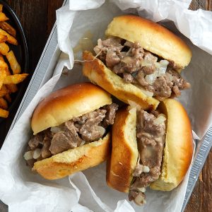 3 philly cheesesteak sliders in a metal pan with a side of fries.
