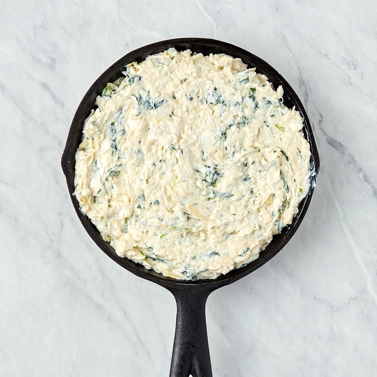 unbaked crab spinach artichoke dip in a skillet.