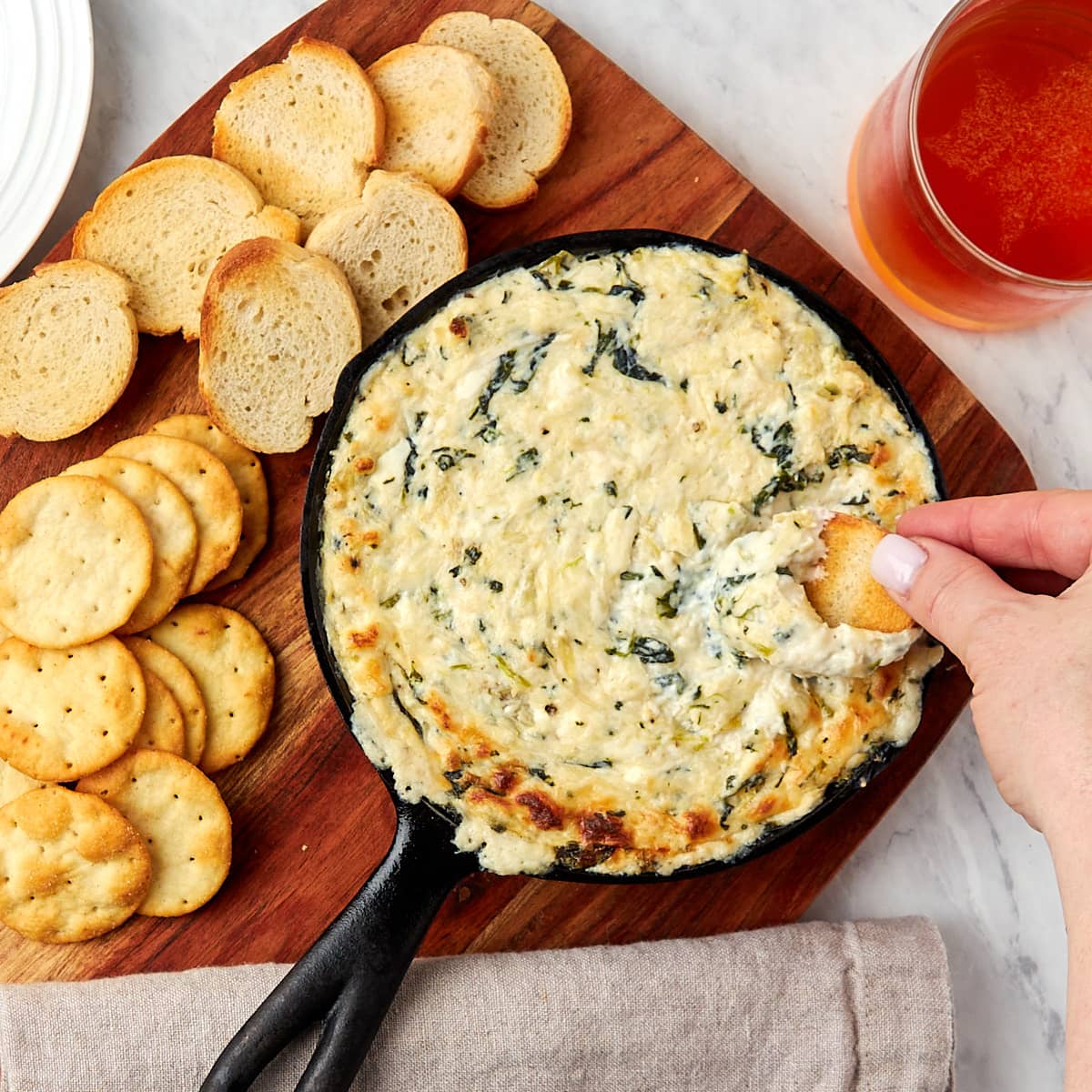 baked crab spinach artichoke dip in a skillet served with of crostini and crackers.