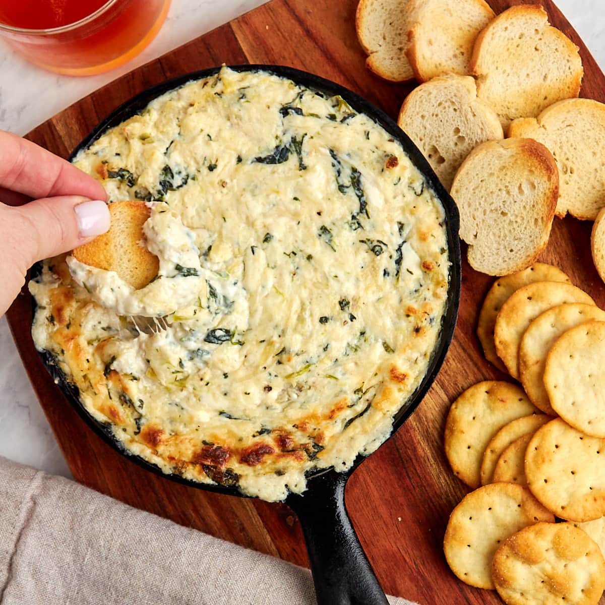 baked crab spinach artichoke dip in a skillet served with of crostini and crackers.