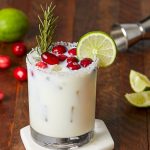 white christmas margarita garnished with lime, cranberries, and a sprig of rosemary.