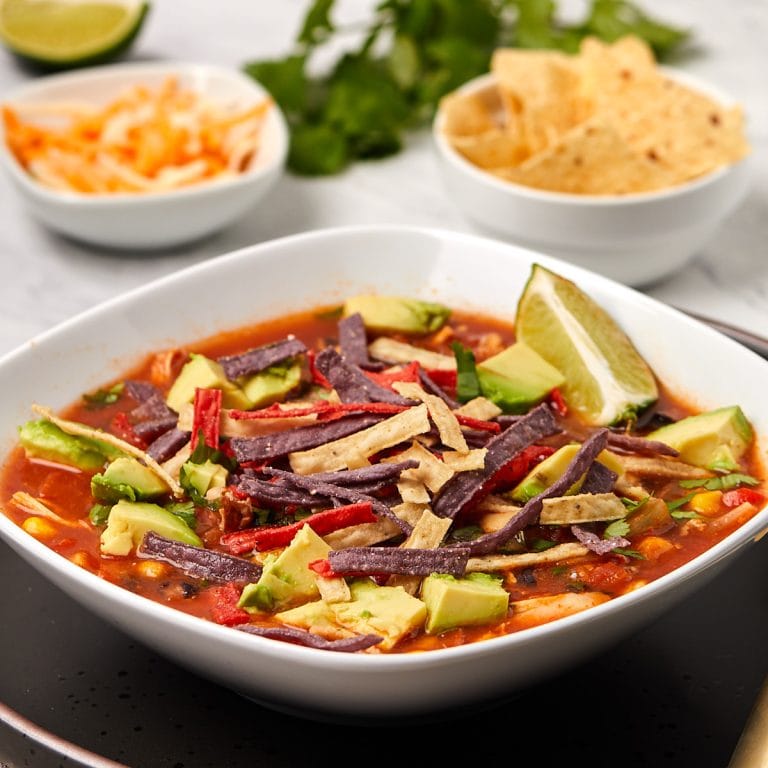 chicken tortilla soup topped with avocado and lime in a bowl.