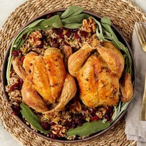cooked cornish game hens on a plate with extra wild rice stuffing.