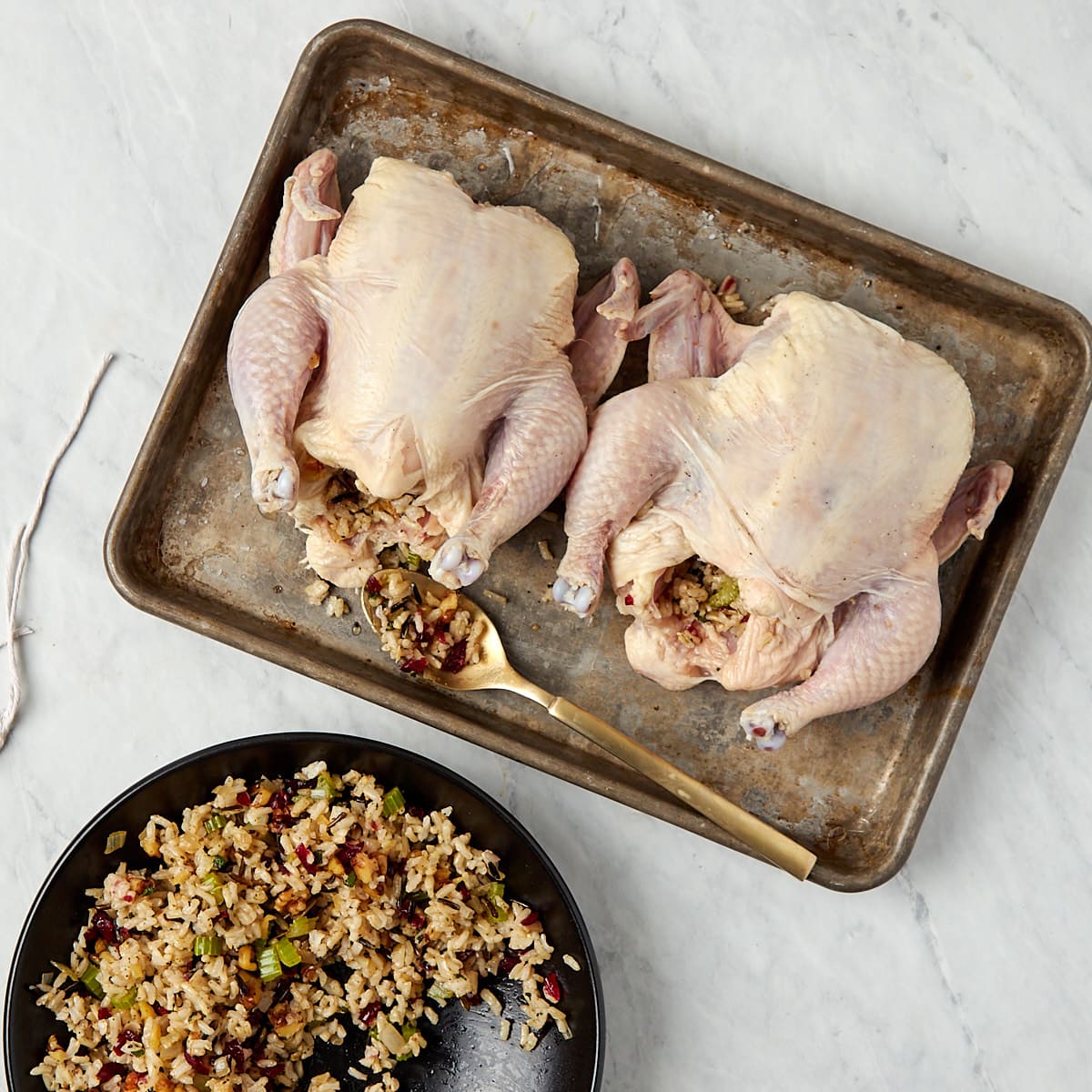 cornish game hens on a baking sheet being stuffed with wild rice stuffing.