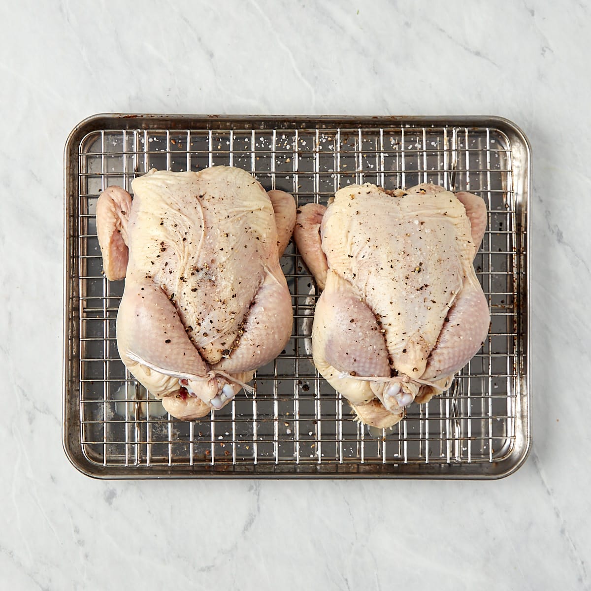 stuffed uncooked Cornish game hens on a wire rack-lined baking pan.