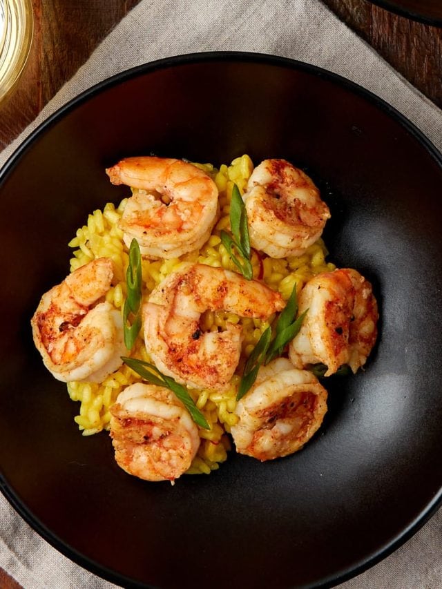 saffron shrimp risotto served in a black bowl with 6 cooked shrimp on top.