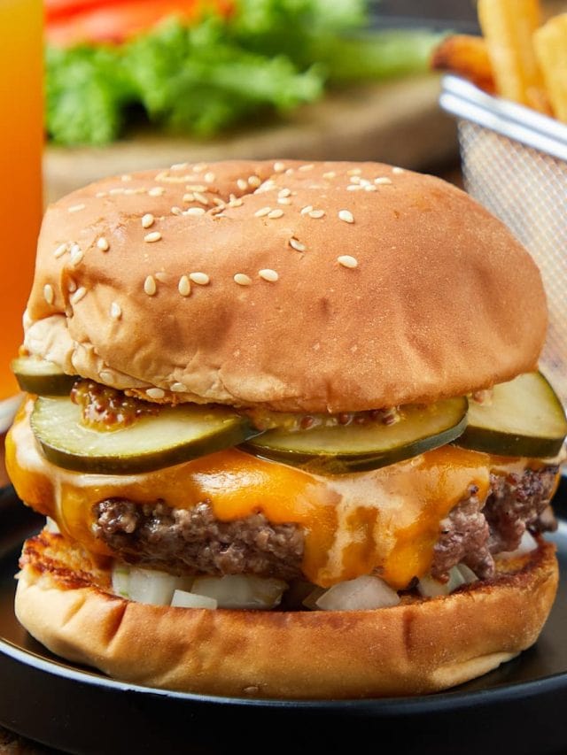 cheeseburger with onions, pickles, and mustard on a black plate.
