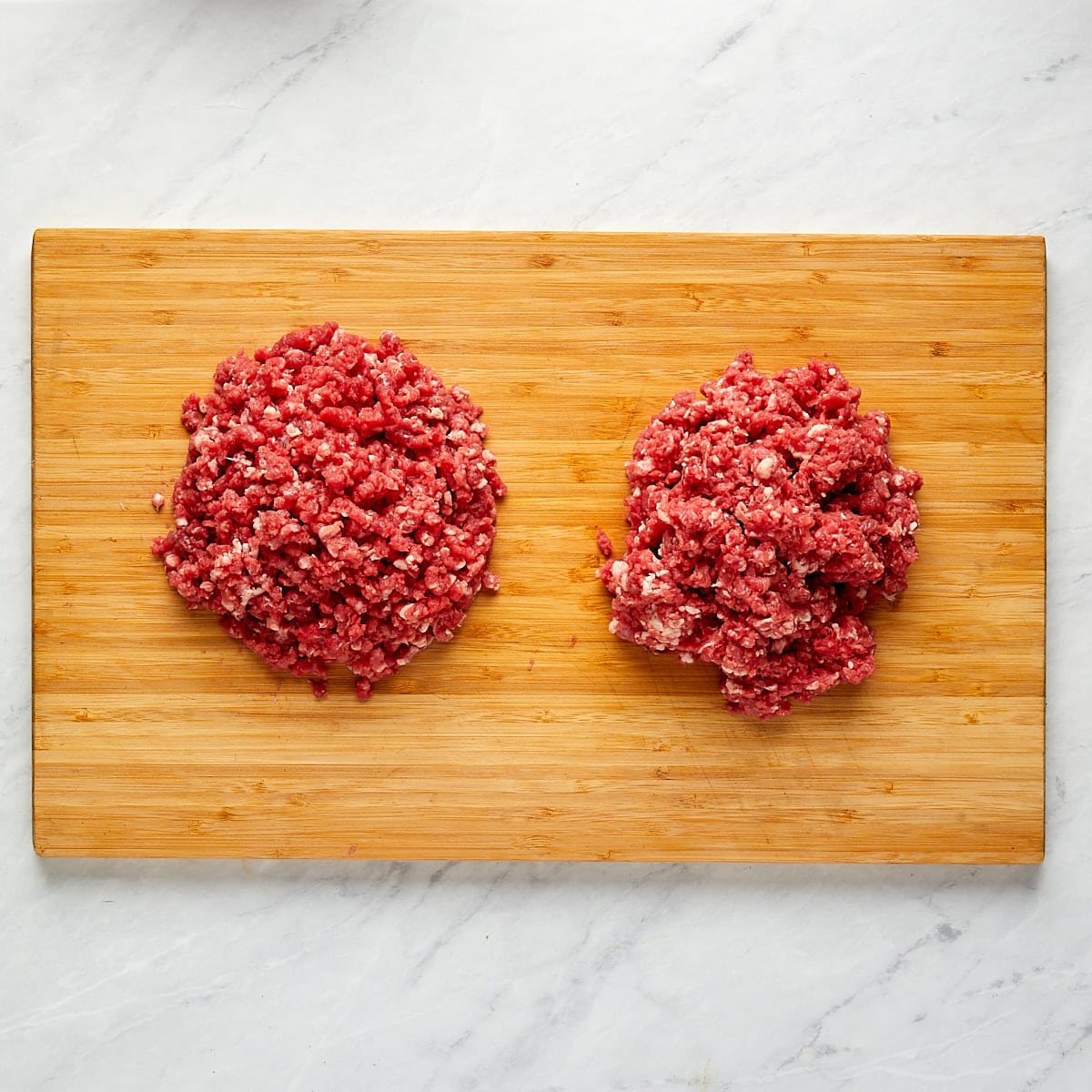 beef that has been ground with a kitchen-aid stand mixer with grinder attachment and beef that has been ground with food process sitting side by side on a wood cutting board.