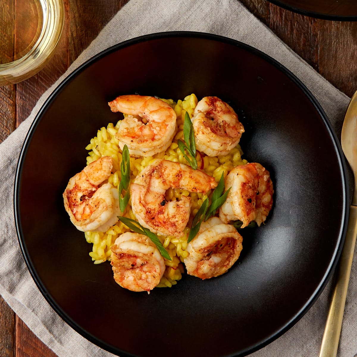 saffron shrimp risotto served in a black bowl with 6 cooked shrimp on top.