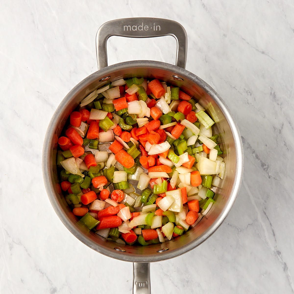the mirepoix of carrots, celery, and onions cooking in a saucepan.