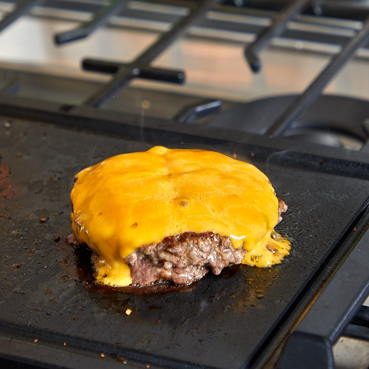 cheese melting on a burger patty as it is being grilled.