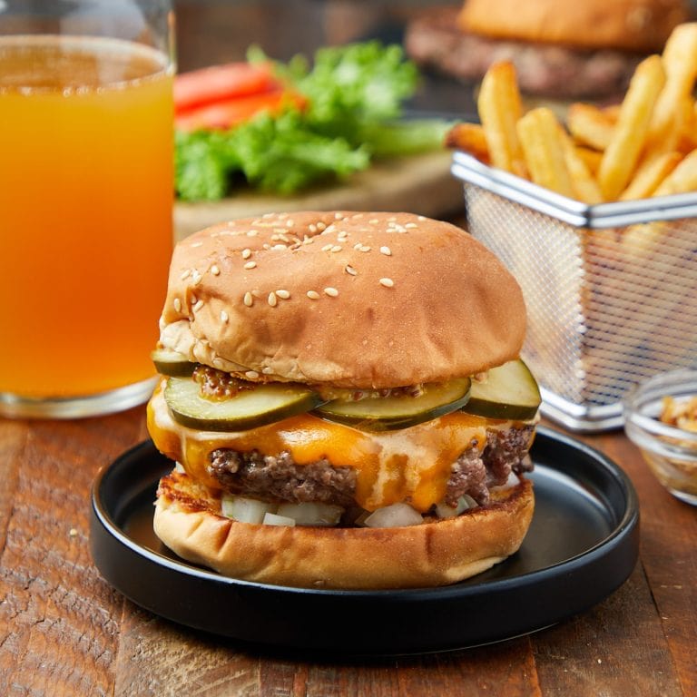cheeseburger with onions, pickles, and mustard on a black plate served with fries and a beer.