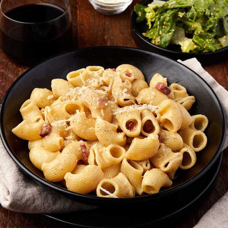 pasta alla gricia in a black bowl served with a sprinkle of grated cheese.