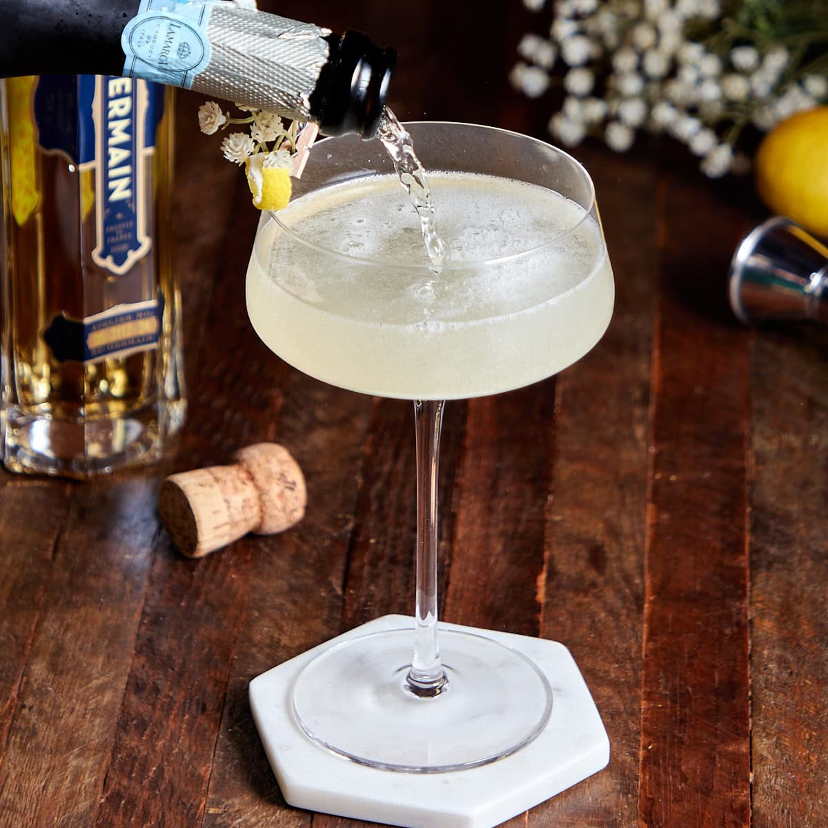 sparkling wine being poured into a coup glass with St-Germain, Gin, and lemon juice.