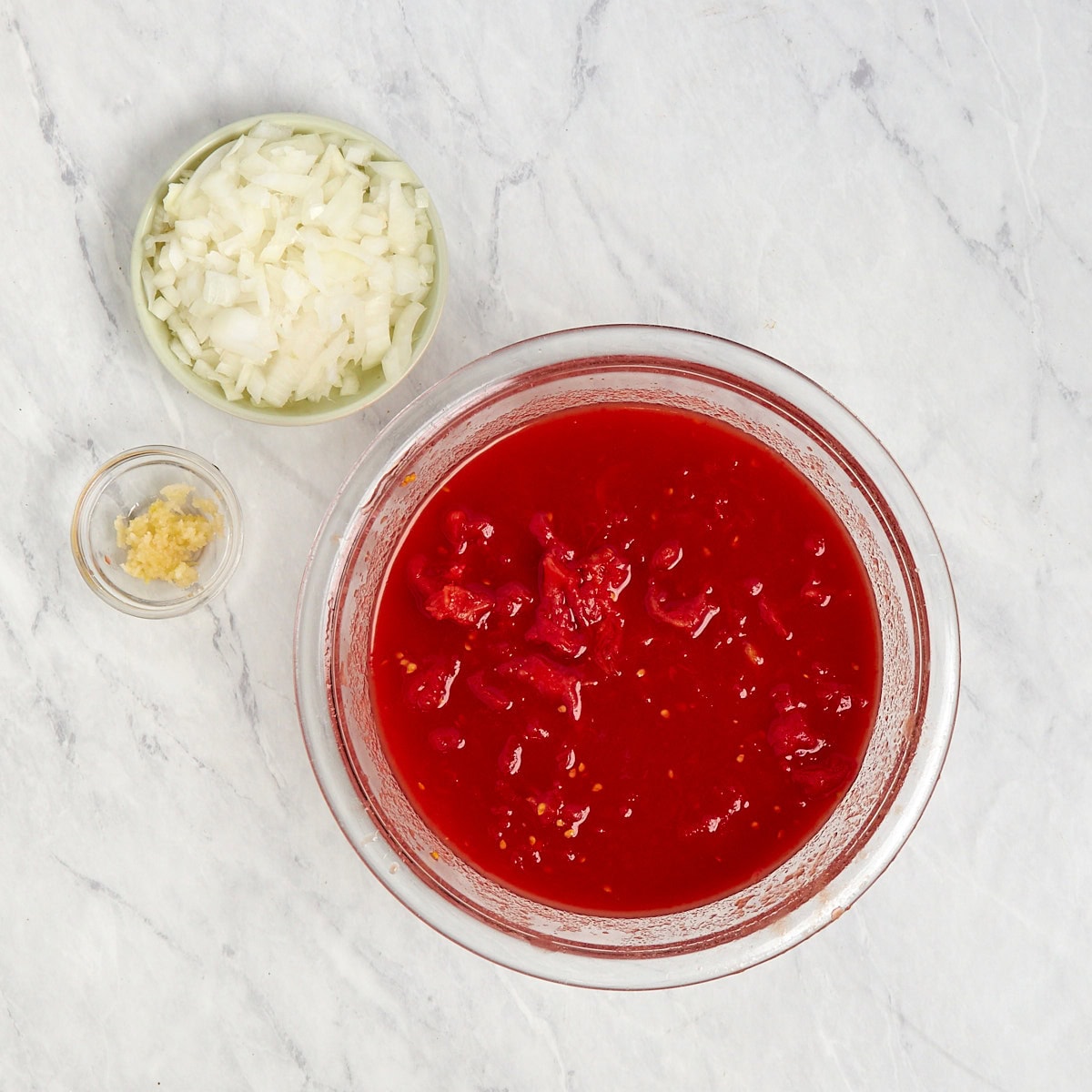 onions, garlic, and tomatoes in bowls prepped for sauce.