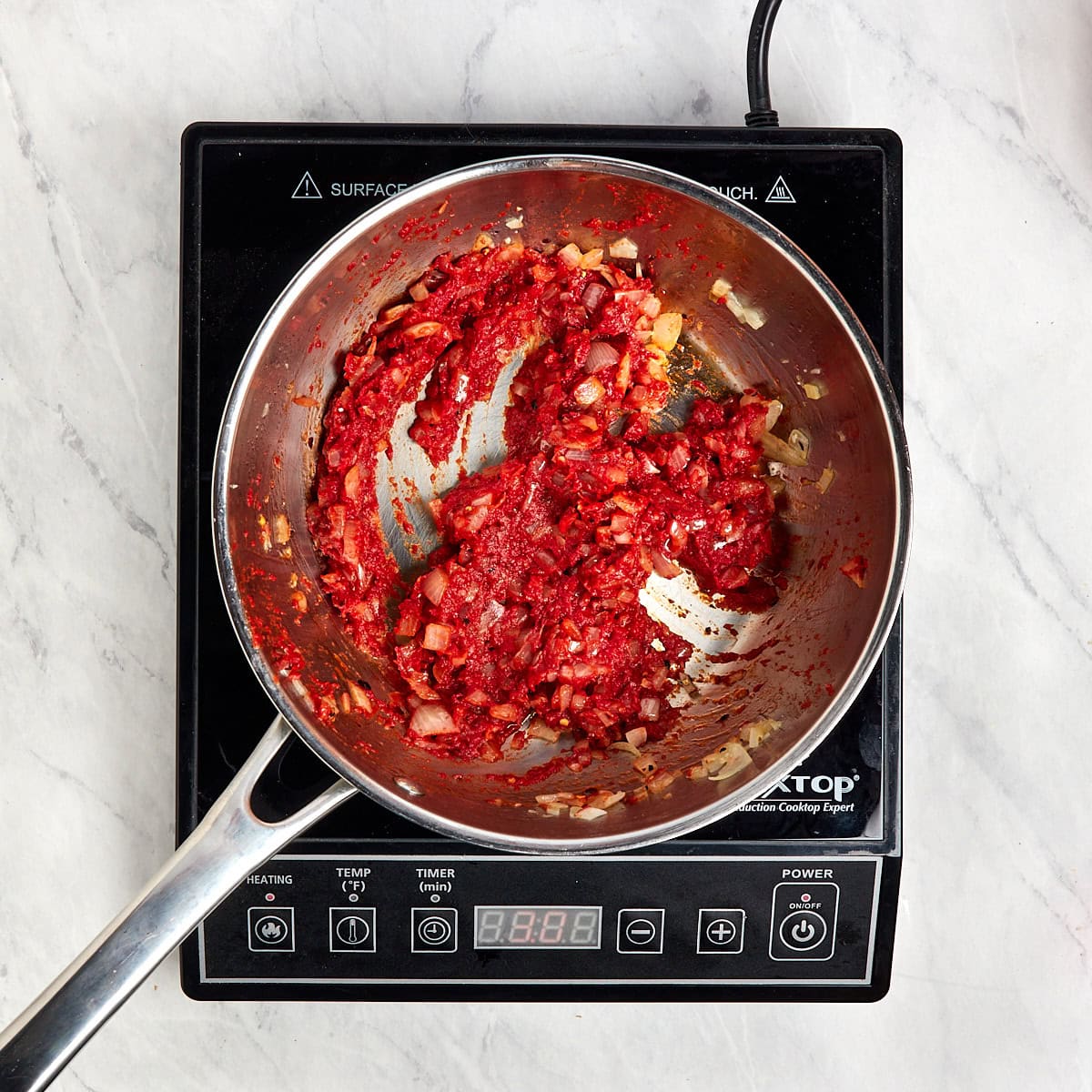 tomato paste cooking in a saucepan with onions.