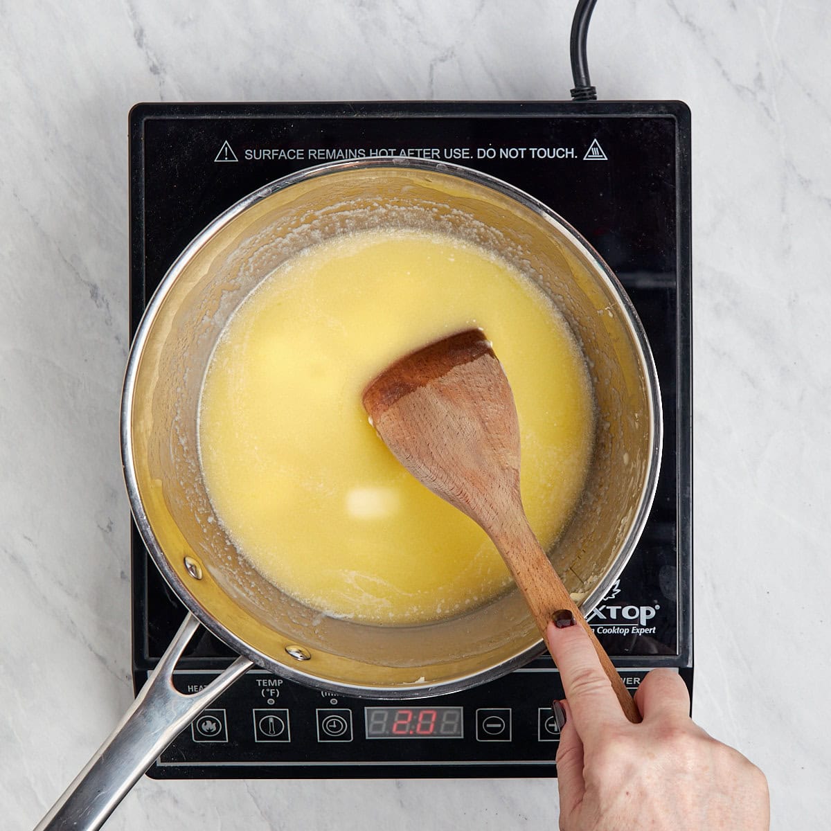 butter being stirred in a metal saucepan as it melts.