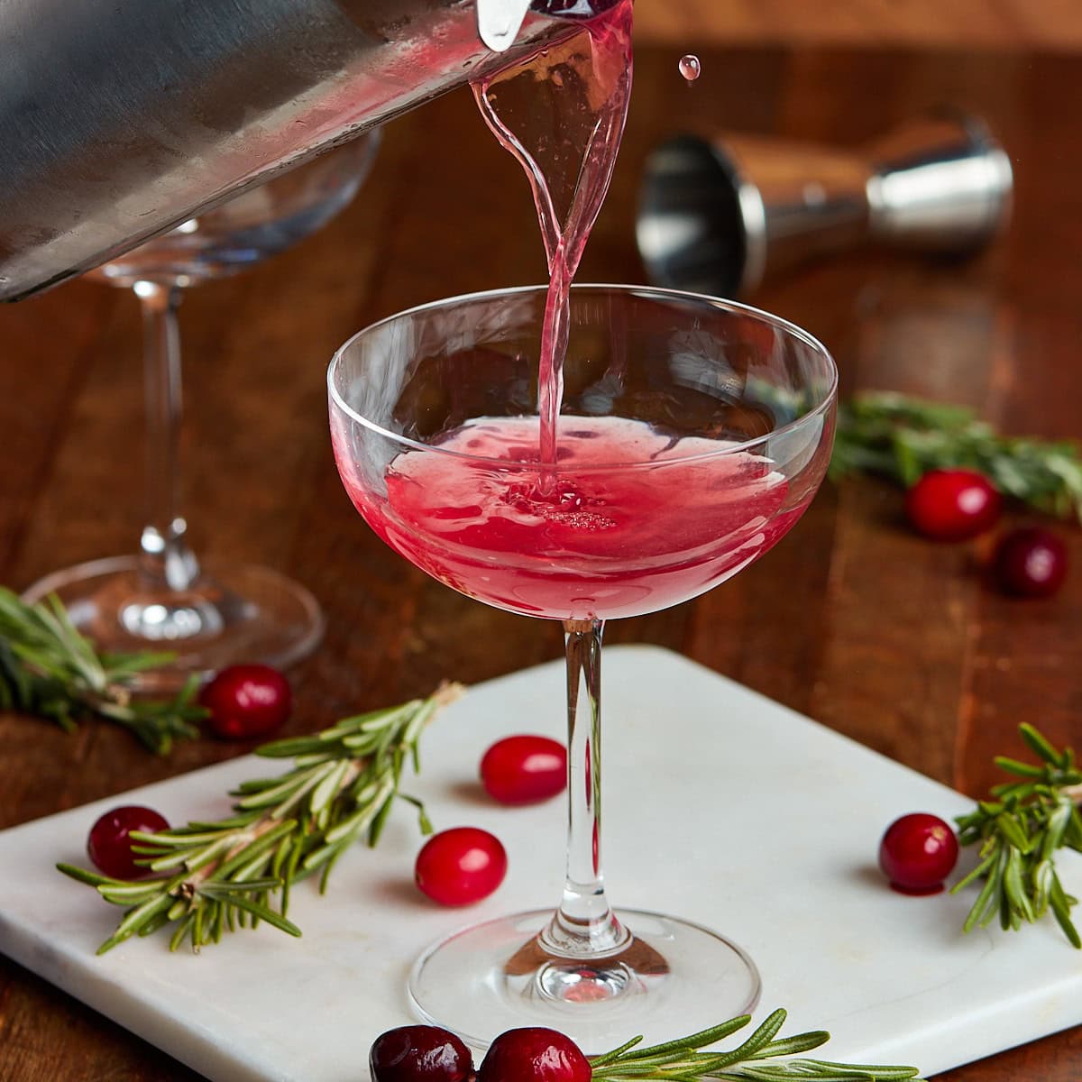 cranberry martini being poured from a cocktail shaker into a coup glass.