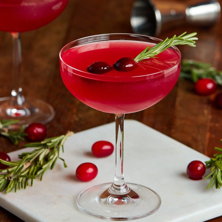 mistletoe martini in a coup glass garnished with rosemary and cranberries.