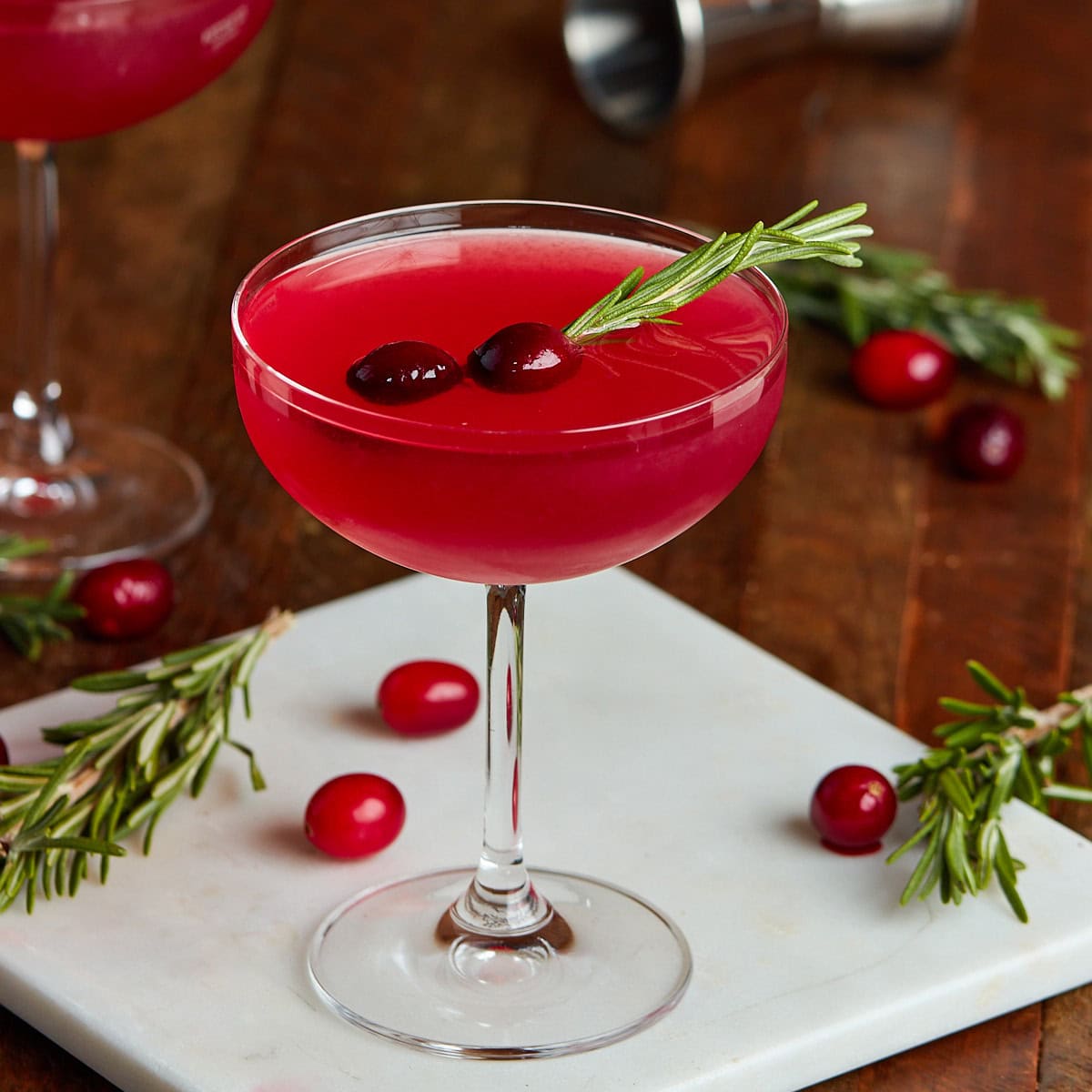cranberry martini in a coup glass garnished with rosemary and cranberries.