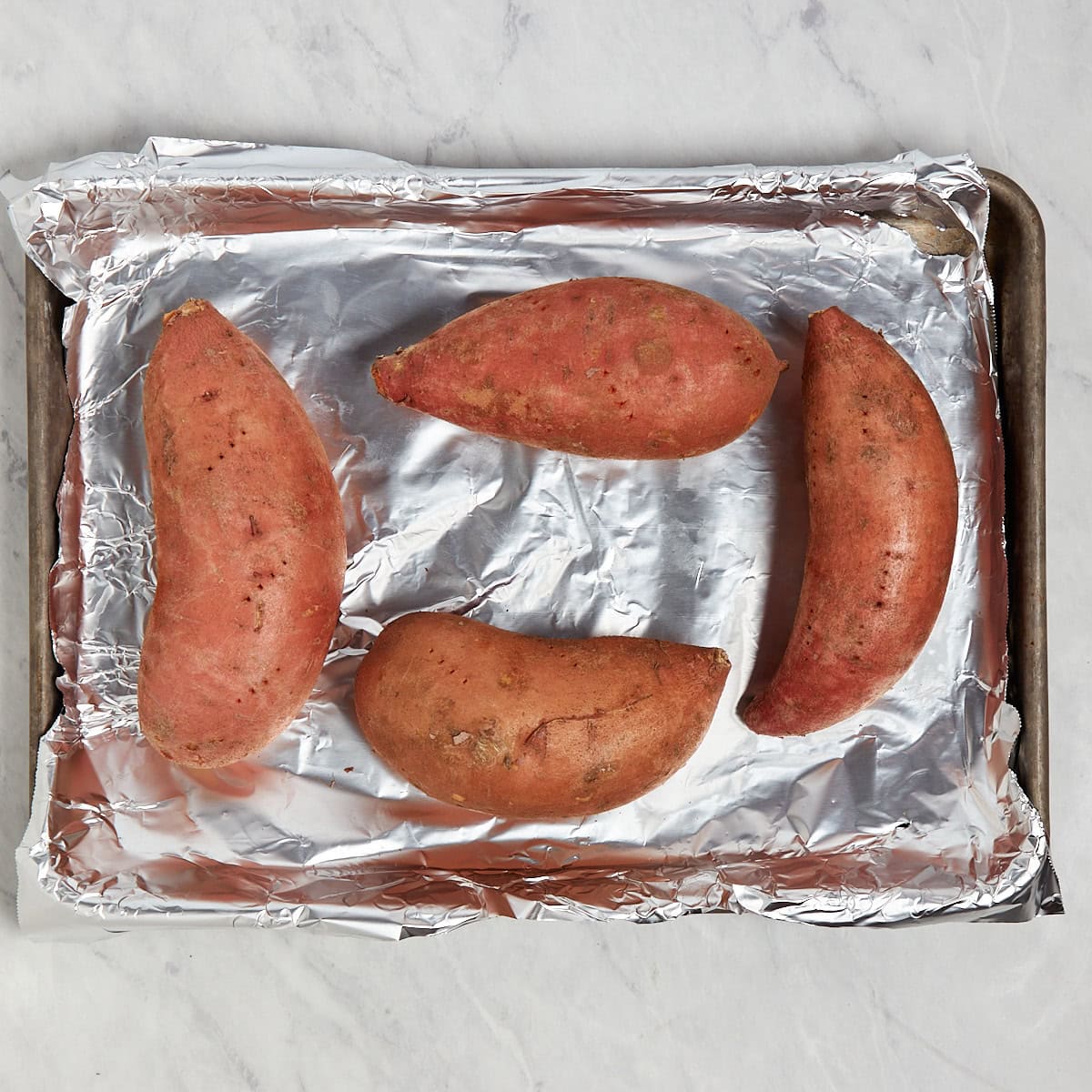 four sweet potatoes that were pierced with a fork on a foil lined sheet tray.