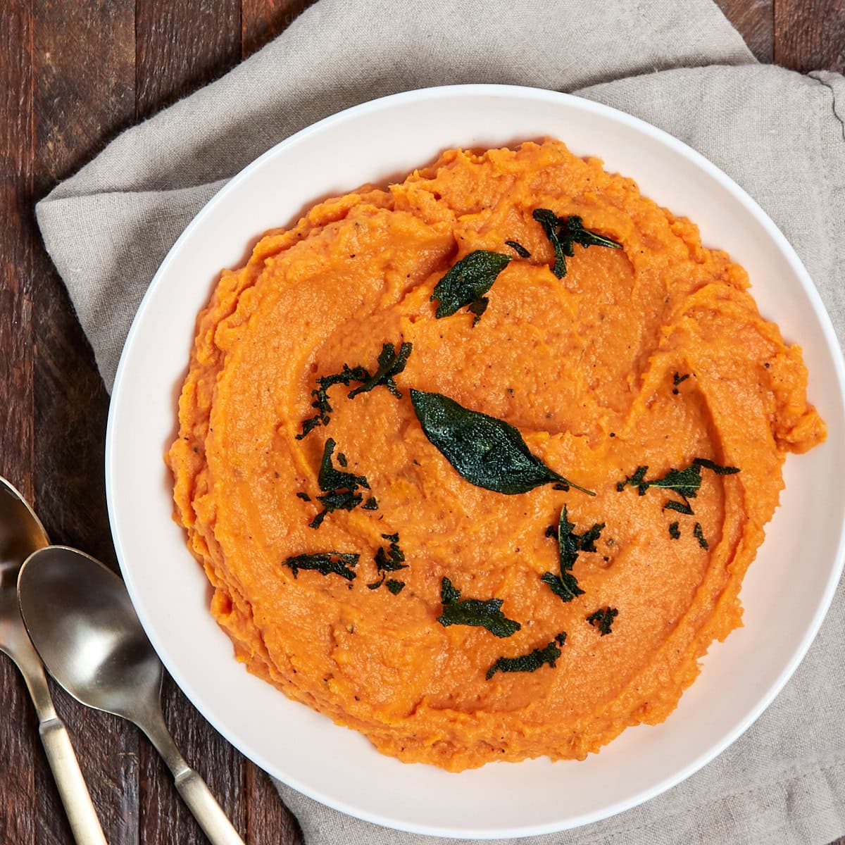 whipped sweet potatoes garnished with fried brown butter sage in a serving bowl.