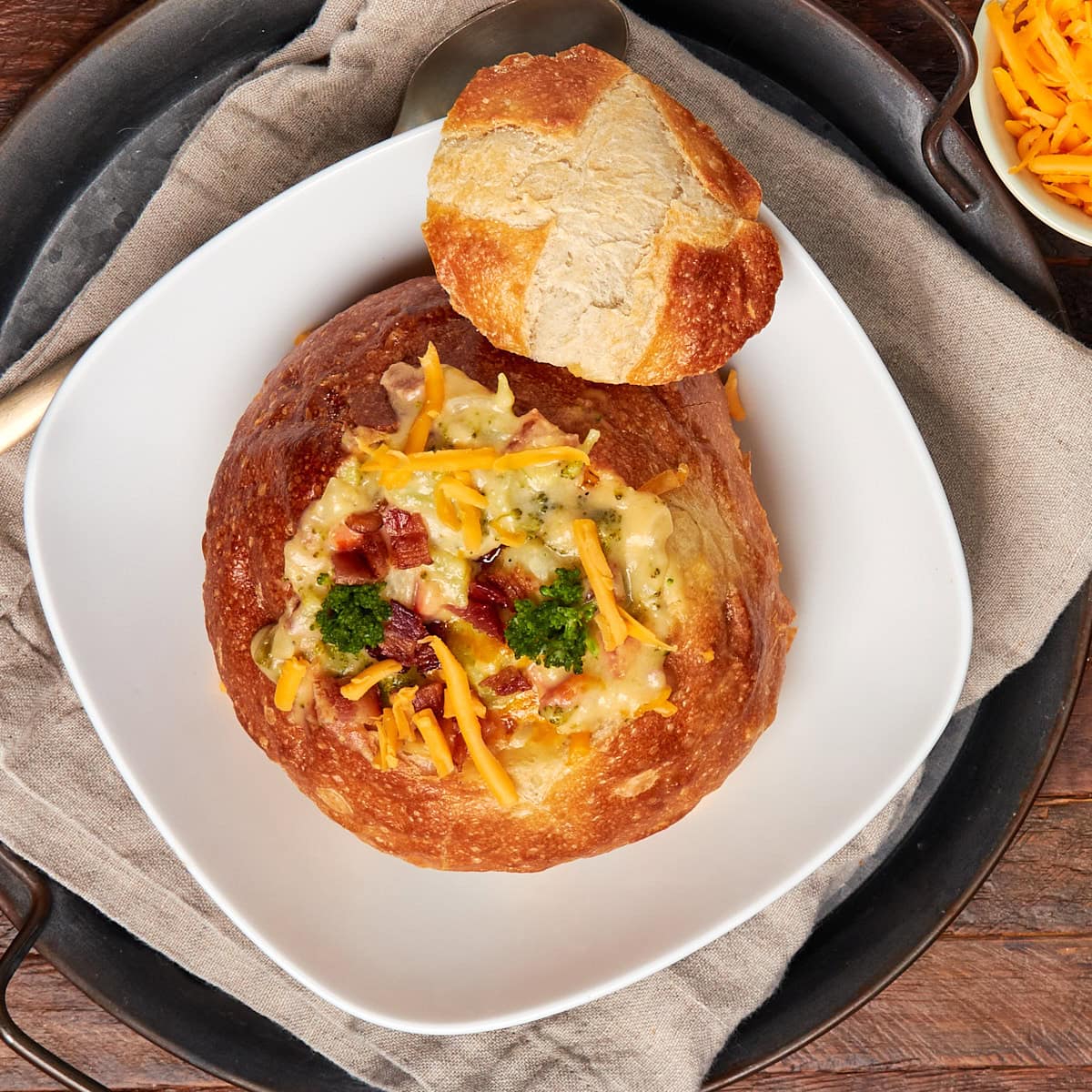 broccoli cheese bacon soup in a bread bowl served in a white bowl.