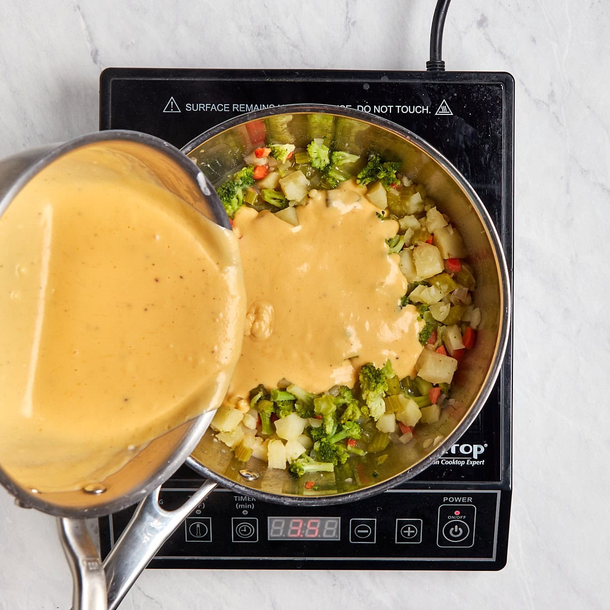 cheese sauce being poured into the vegetable soup base.