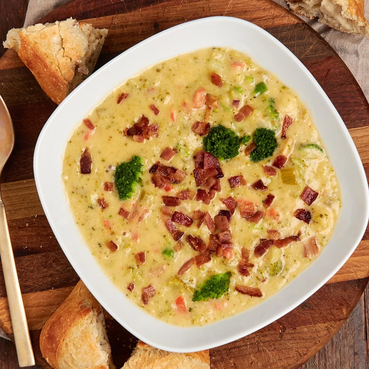 broccoli cheese bacon soup in a bread bowl topped with extra bacon served in a white bowl.