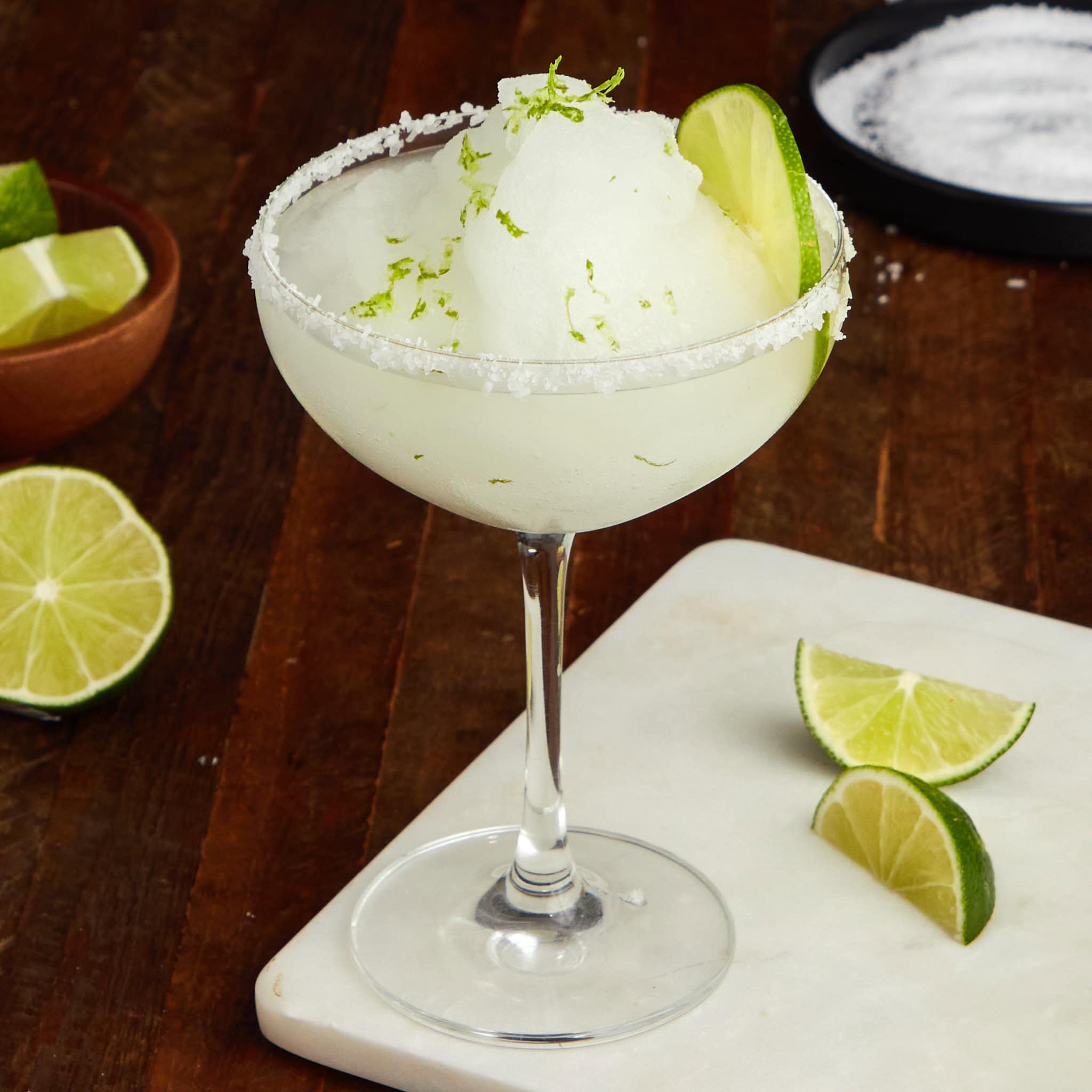 frozen margarita with a salted rim in a coupe glass garnished with a wedge of lime.