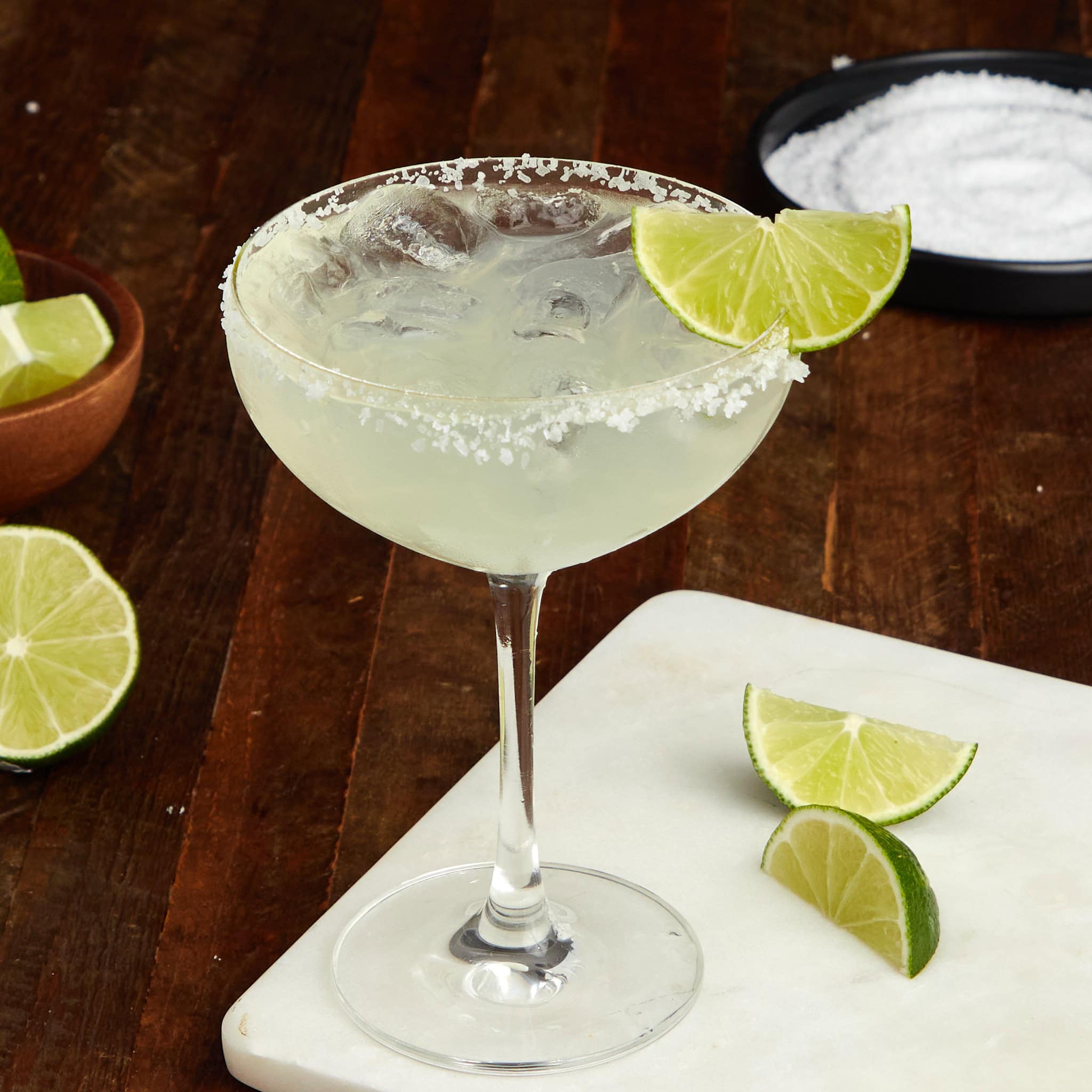 margarita on the rocks with a salted rim in a coupe glass garnished with a wedge of lime.