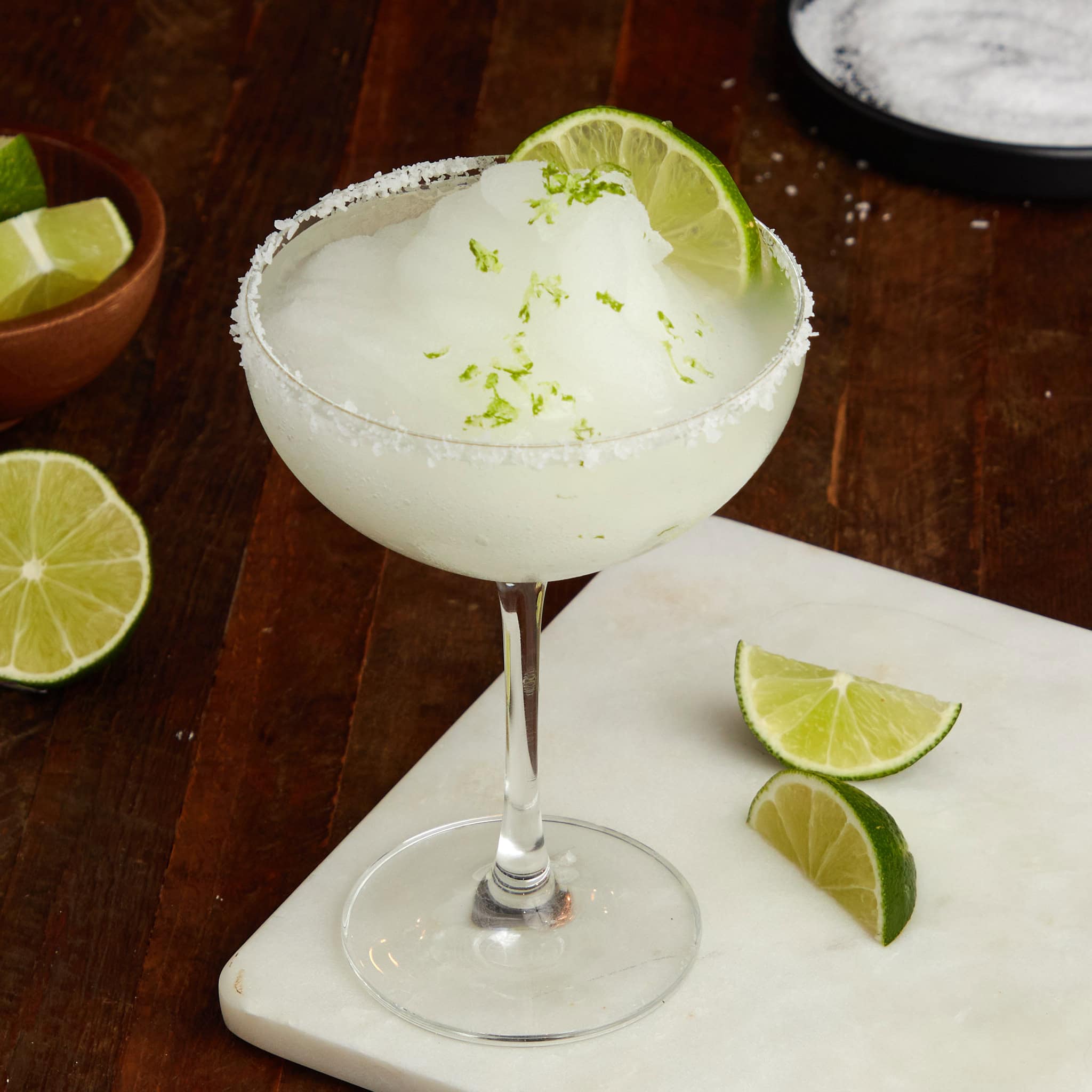 frozen margarita with a salted rim in a coupe glass garnished with a wedge of lime.