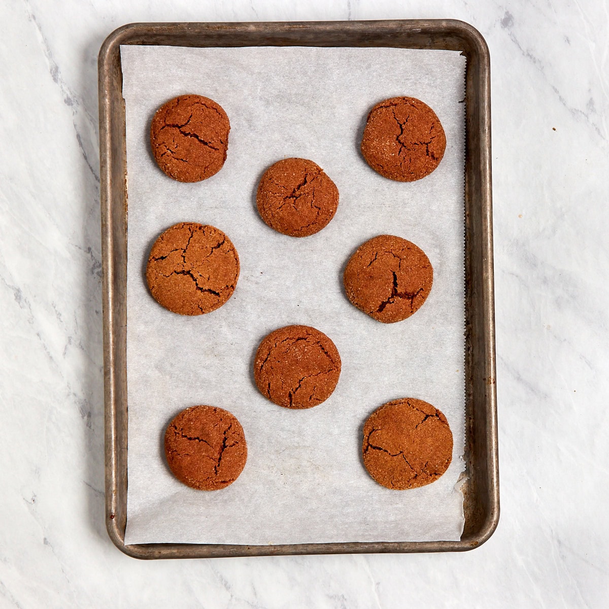 8 cooked ginger cookies on a cookie sheet lined with parchment.