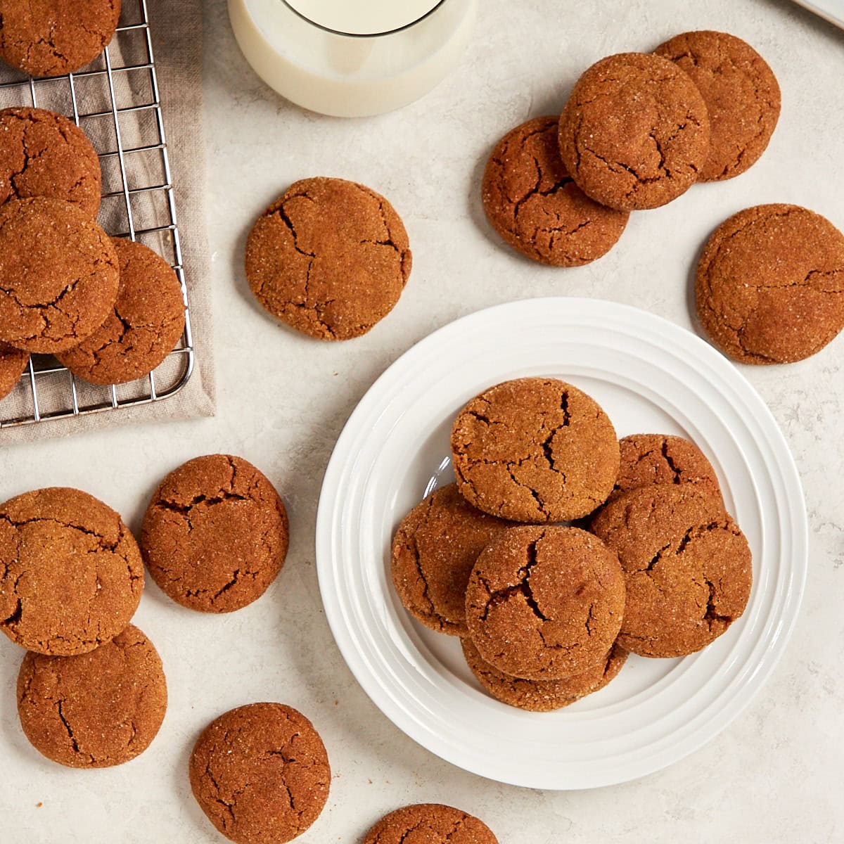 ginger molasses cookies spread out on a table with a plate of cookies and a glass of milk.