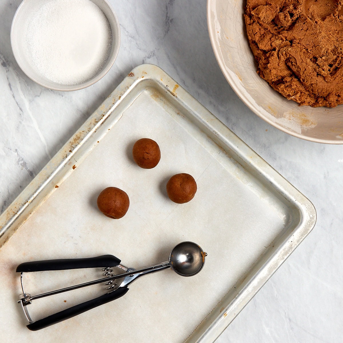 3 uncooked balls of ginger molasses cookies on a parchment lined cookie sheet.