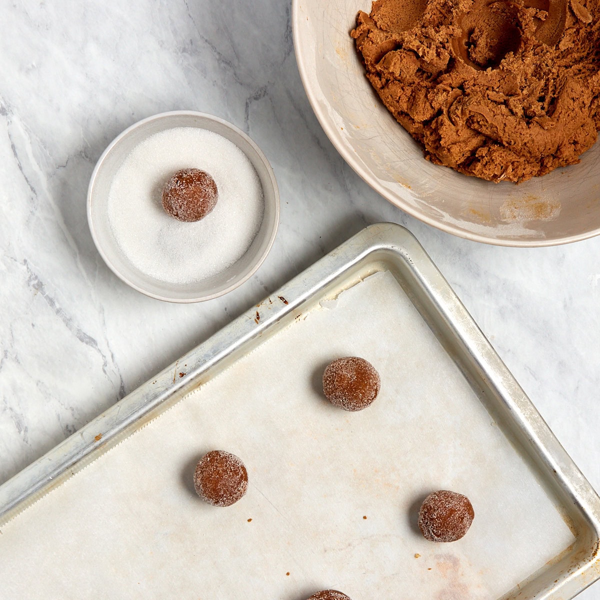 uncooked ginger molasses cookie ball being rolled in a bowl of sugar.