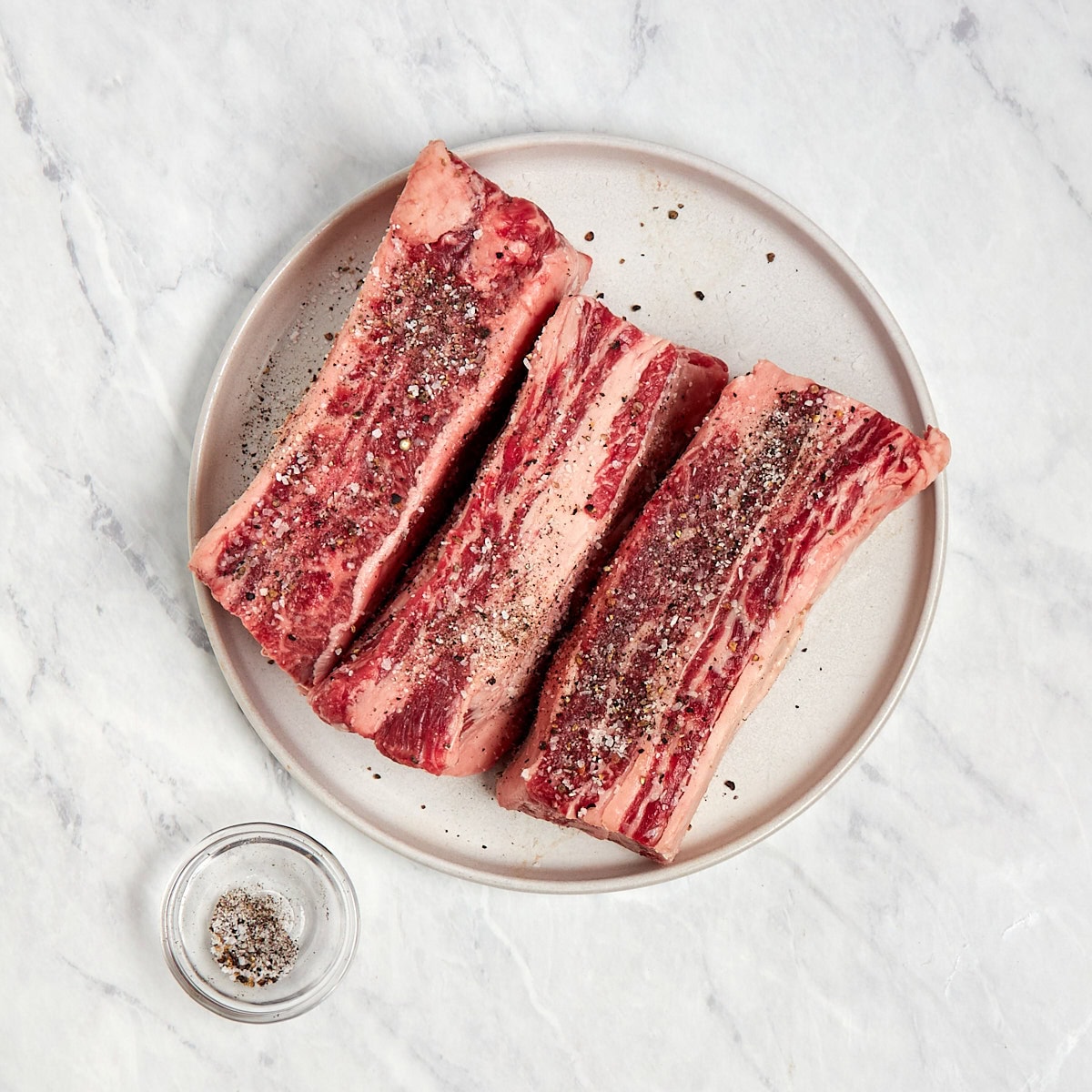 short ribs being seasoned with salt and pepper.