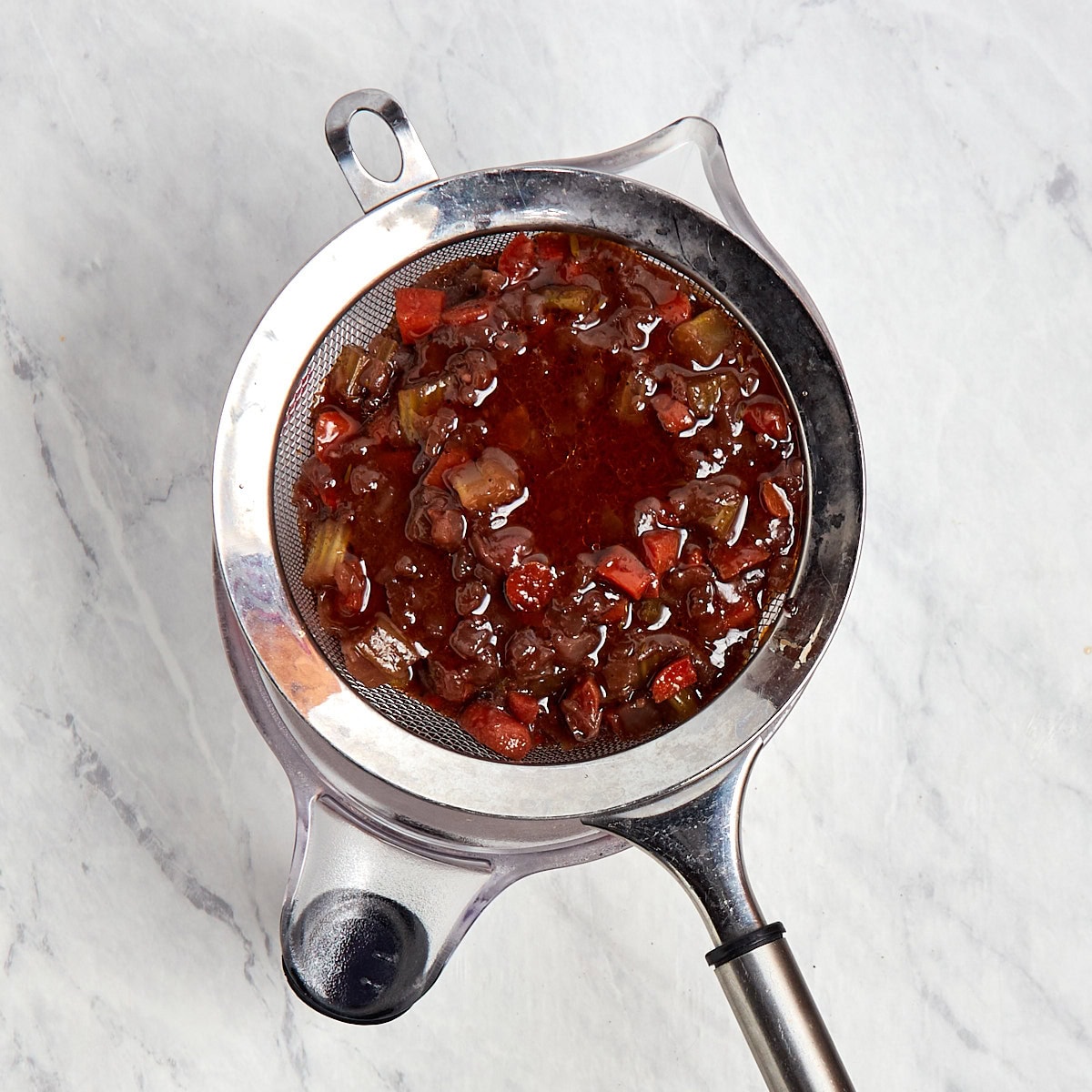 braising liquid being strained through a mesh strainer into a large measuring cup.