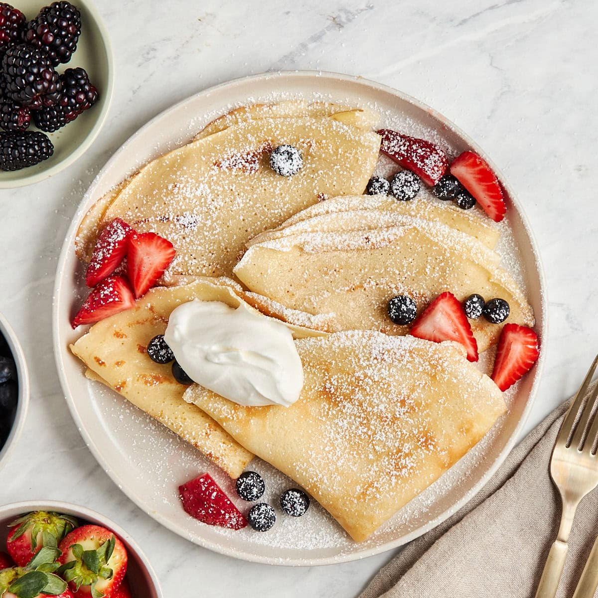 Delicious crepes topped with strawberries, blueberries, and whipped cream, served on a white plate.