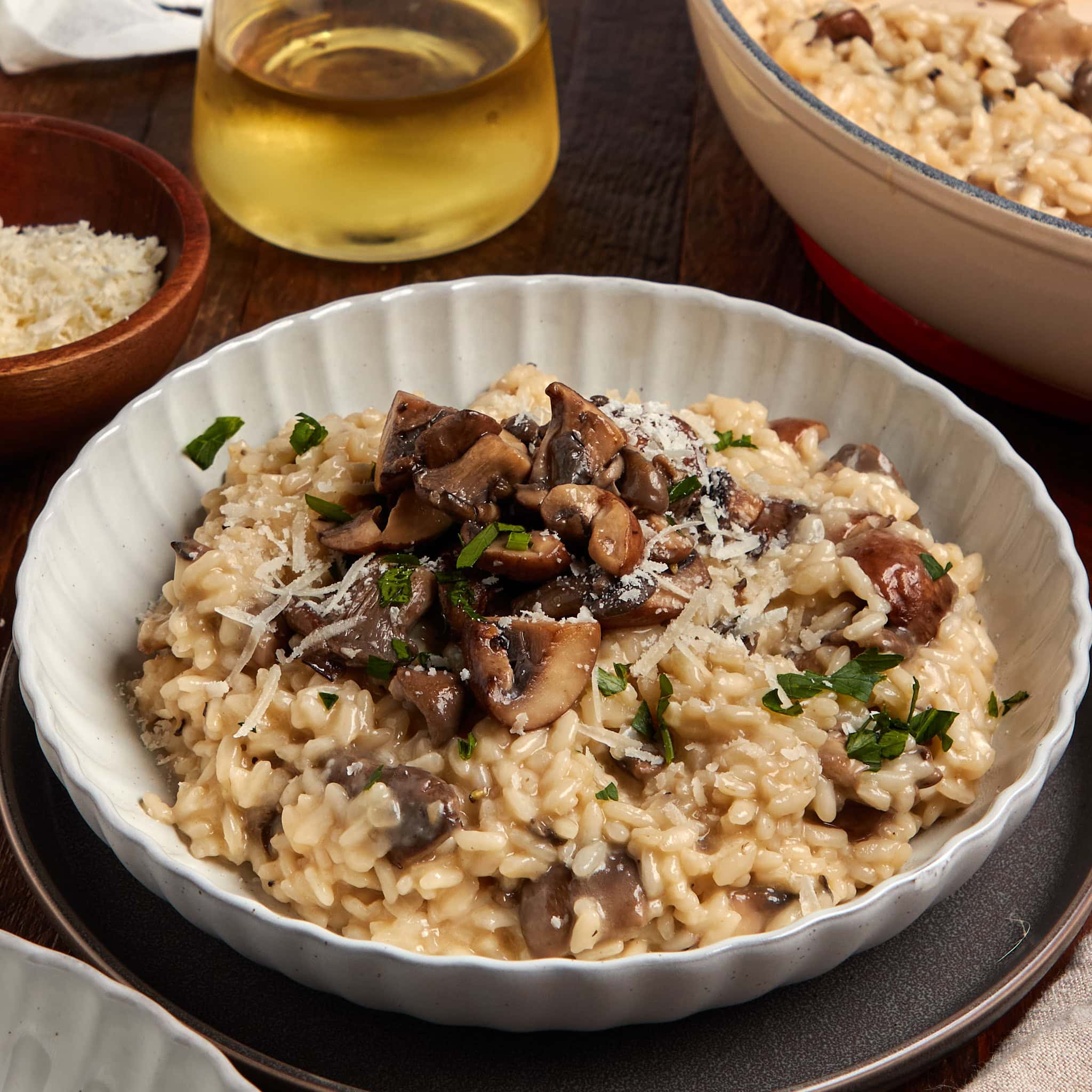 mushroom truffle risotto in a white bowl topped with chopped parsley and extra cheese.
