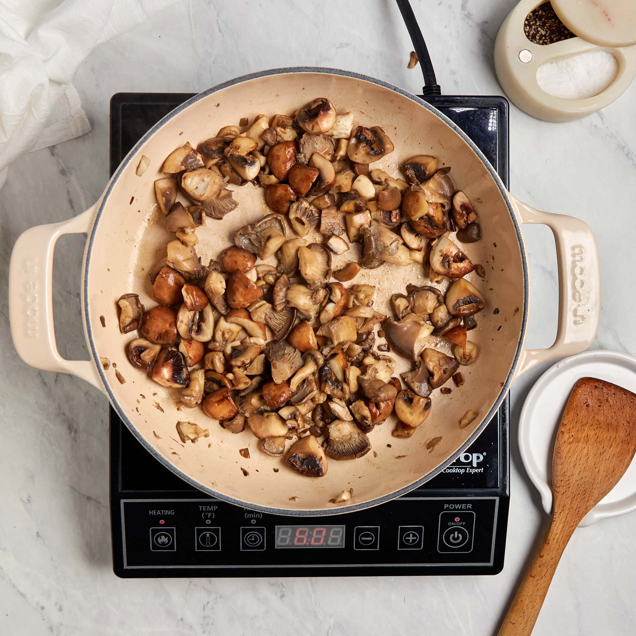mushrooms sautéing in a white braiser on a portable induction cooktop.