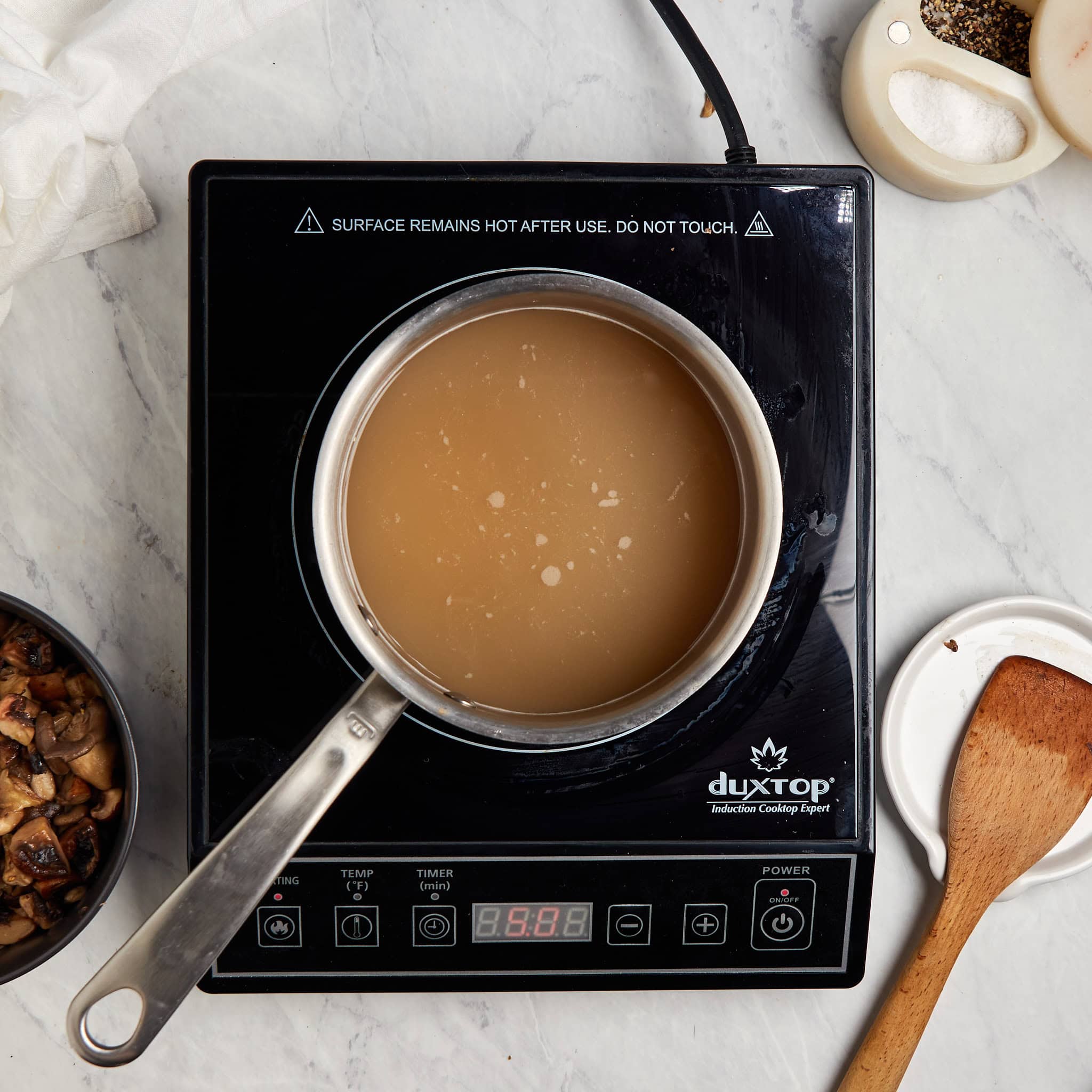 chicken stock warming in a saucepan on a portable induction cooktop.