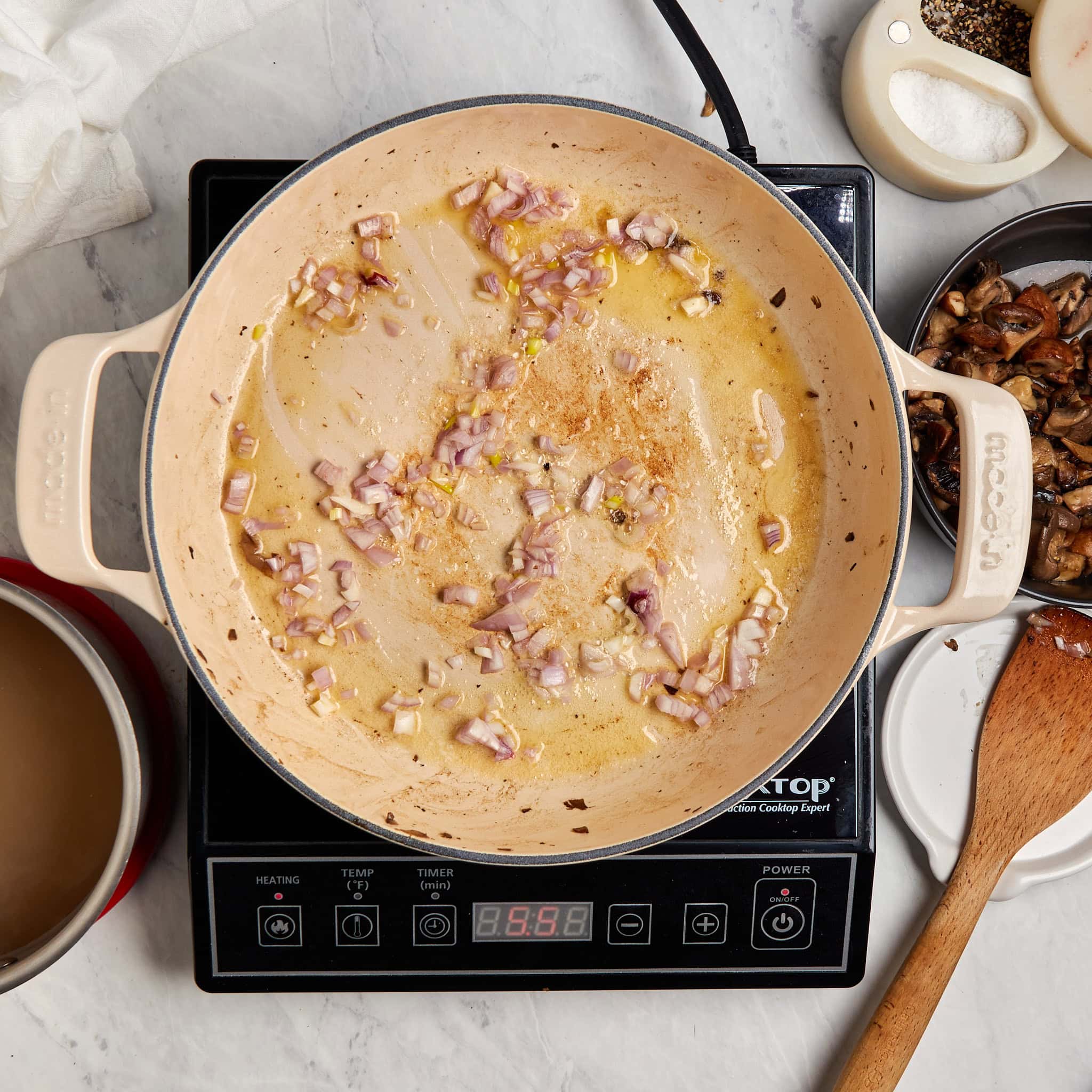 shallots sautéing in a braiser on a portable induction cooktop.