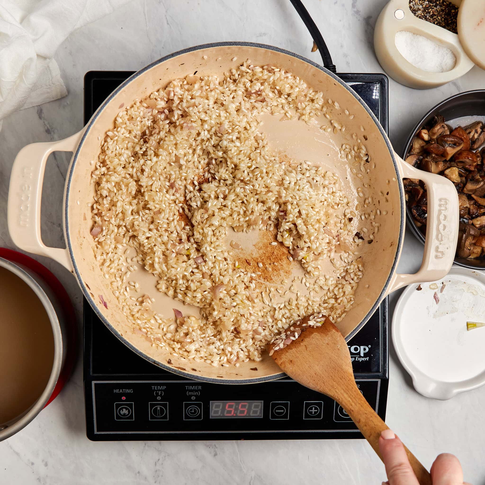 arborio rice being coated in oil in a braiser on a portable induction cooktop.